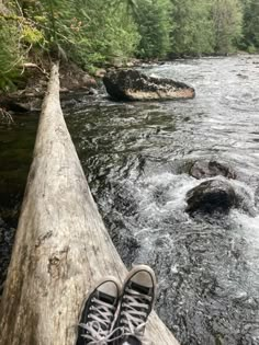 someone is standing on a log in the middle of a river with their feet up