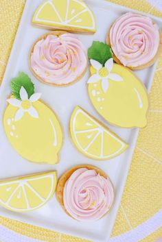 lemon cookies decorated with pink icing on a white plate next to sliced lemons