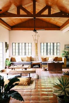 the inside of a living room with couches, tables and plants on the floor