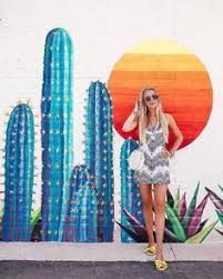 a woman standing in front of a cactus mural with her hands on her head and wearing sunglasses