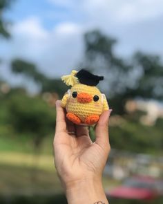 a hand holding a small yellow stuffed animal with a black hat on it's head