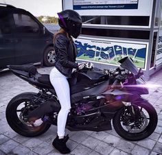 a woman in white pants and black jacket sitting on a motorcycle next to a van