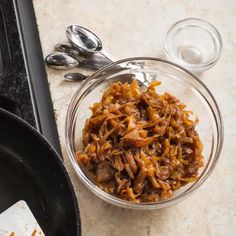 a glass bowl filled with food on top of a counter next to a frying pan