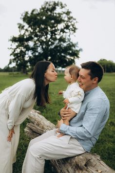 a man and woman holding a baby while sitting on a log