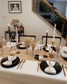 the table is set with black and white plates, silverware, gold candlesticks