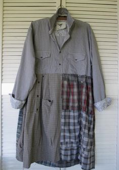 a shirt dress hanging on a wall with white shutters in the background and an open door behind it