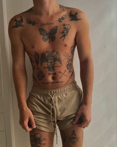 a man with many tattoos on his body and chest standing in front of a white wall