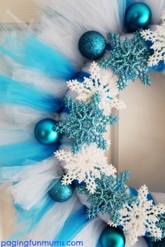 a blue and white christmas wreath with snowflakes, ornaments and tulle on it