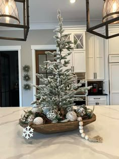 a white christmas tree in a wooden bowl on a kitchen counter with lights hanging from the ceiling