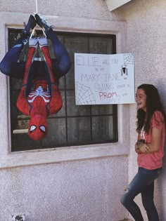 a woman standing next to a window with a spiderman sign hanging from it's side