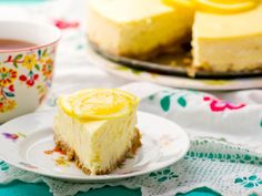 a slice of lemon cheesecake on a plate with a cup of tea in the background