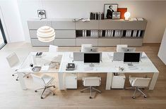 an office desk with four computers on it in front of a bookcase and large window