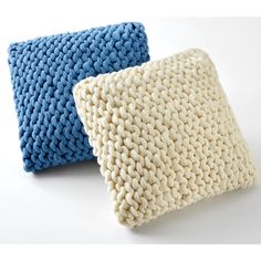 two knitted pillows sitting next to each other on a white surface with one blue and one beige