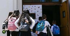 several children with backpacks are standing in front of the door to an open building