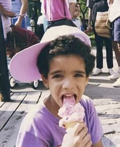 a young child wearing a pink hat eating an ice cream cone