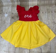 a yellow and red dress with the word one on it sitting on a wooden floor