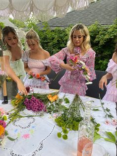 three women standing around a table with flowers on it