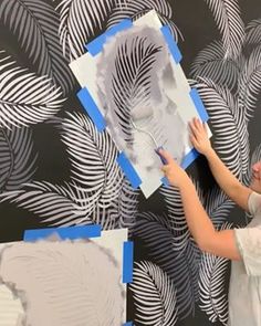 a woman is painting a wall with blue tape and white feathers on the wall behind her