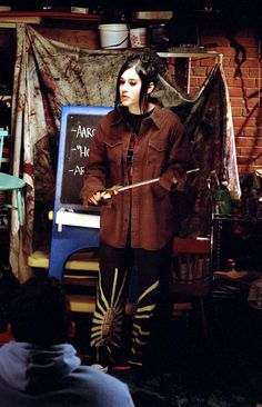 a woman standing in front of a blackboard with writing on it and holding a wand