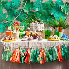 a table topped with lots of food next to a green leafy tree filled wall