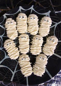 halloween treats with white icing and eyes on a black plate next to spider webs