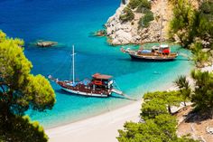 two boats are anchored in the clear blue water near an island with white sand and green trees