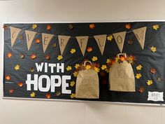 a bulletin board with two brown paper bags hanging from it's sides and fall leaves on the wall