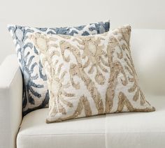 two pillows on a white couch with blue and beige patterns in the back, side view