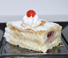 a piece of cake sitting on top of a black plate covered in whipped cream and cherries