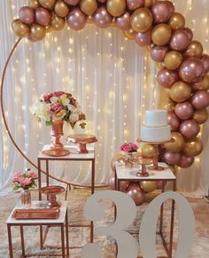 a table topped with two tables covered in gold and pink balloons next to a cake