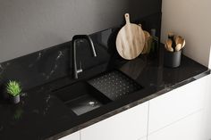 a kitchen sink with black counter top and wooden utensils on the countertop