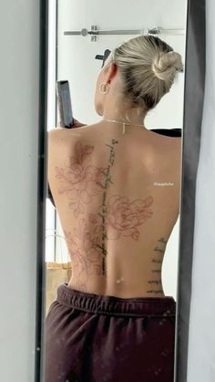 a woman with tattoos on her back looking at herself in the mirror and holding a cell phone