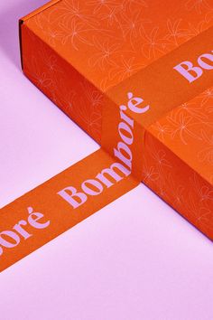 two orange boxes with white lettering on them sitting next to each other in front of a pink background