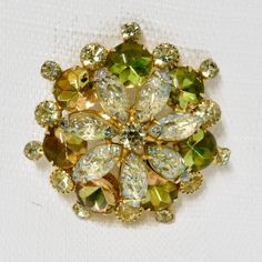 a brooch with green and yellow stones in it's center on a white surface