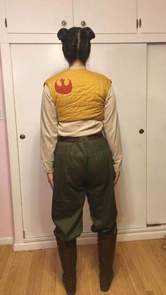 a woman standing in front of white cupboards wearing a star wars vest and brown boots