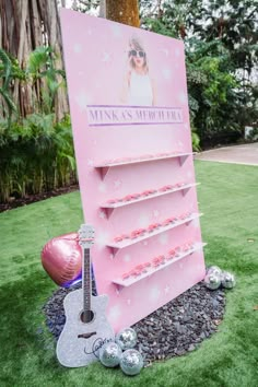 a pink sign that has a guitar and some balls in front of it on the grass