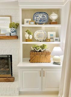 a white bookcase with blue and white plates on it, next to a fireplace