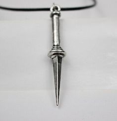 a silver necklace with a long pointed blade hanging from it's center, on a black cord