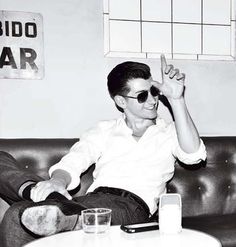 a black and white photo of a man sitting on a couch with his hand in the air