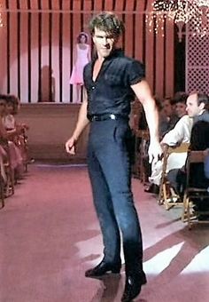 a man is walking down the runway at a fashion show with other people sitting in chairs behind him