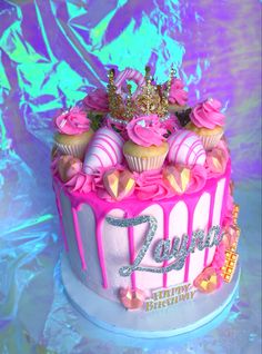 a birthday cake decorated with pink frosting and gold crown on top, sitting on a shiny surface