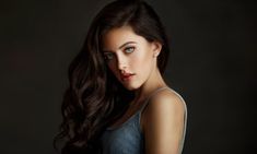 a woman with long dark hair and blue eyes is posing for a studio photo in front of a black background