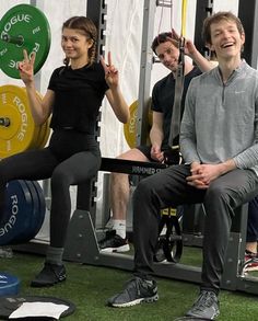 a man and woman sitting on top of a bench in front of a barbell