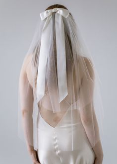 the back of a woman wearing a white veil with an attached bow on her head