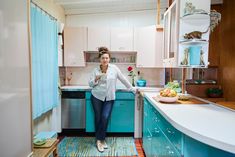 a woman is standing in the kitchen looking at her cell phone while holding a cup