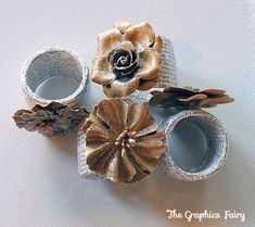 three rolled up paper flowers sitting on top of each other next to some pine cones