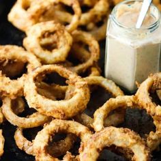 some onion rings are on a black plate with a jar of ranch dressing next to it