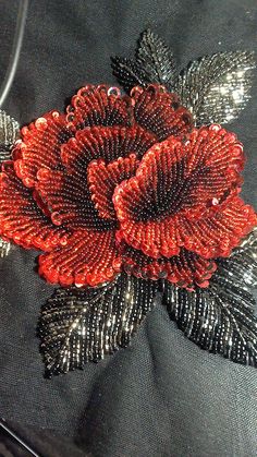 a close up of a red flower on a black fabric material with sequins