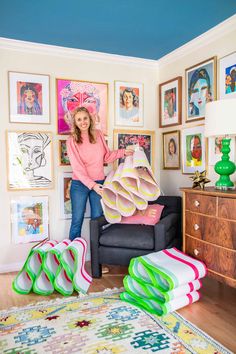 a woman standing in her living room holding up some large pieces of art on the wall