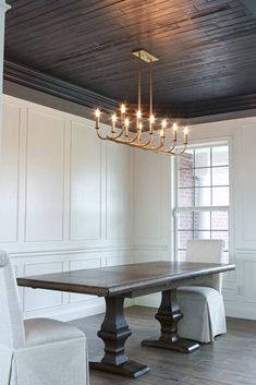 a chandelier hanging from the ceiling in a dining room with white walls and wood flooring